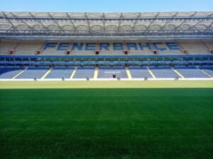 Empty Şükrü Saracoğlu Stadium with green pitch in Istanbul, Türkiye, under clear blue sky.