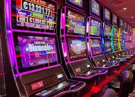 Colorful slot machines lined up in a casino with neon lights and jackpot displays.